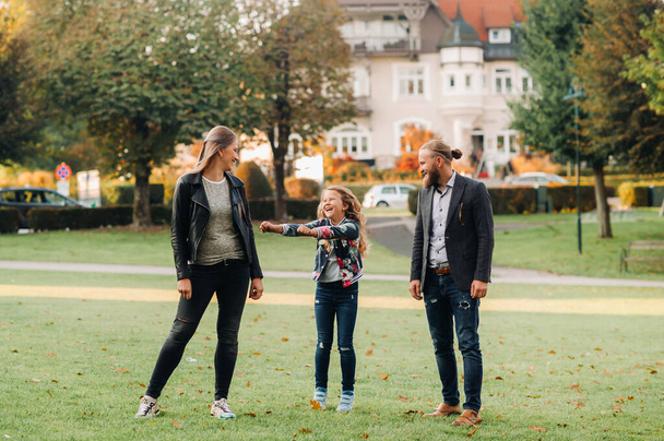 Una familia feliz de tres corre a través de la hierba en el casco antiguo de Austria.Una familia camina a través de una pequeña ciudad en Austria.Europe.Velden am werten Zee. - Foto, imagen