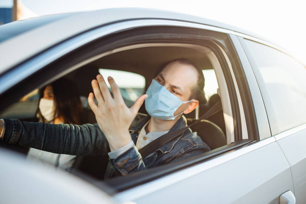 Jongeman boos rijdt een auto met een passagier tijdens een coronavirus pandemie. Taxi chauffeur draagt een masker zeven achter het stuur. Sociale afstand, epidemie, bescherming, gezondheidsconcept - Foto, afbeelding
