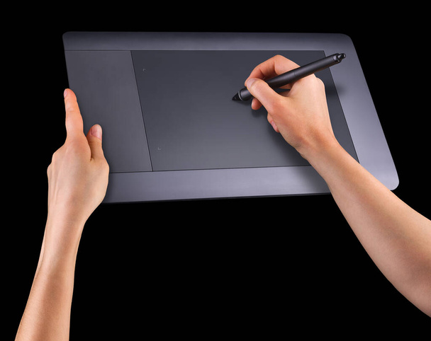 Hand holding digital graphic pen and drawing graphic tablet isolated on black - Photo, image