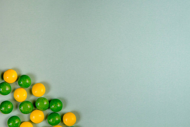 Jasnozielone tło z okrągłym żółtym i zielonym cukierkiem w lewym dolnym rogu. Widok z góry z miejsca kopiowania - Zdjęcie, obraz