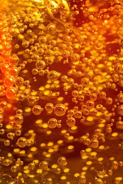 Bekijk van dichtbij de ijsblokjes in oranje soda achtergrond. Textuur van verkoelende zoete zomerdrank met schuim en macro belletjes op de glazen wand. - Foto, afbeelding