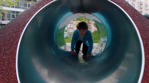 Ένα μικρό αγόρι παίζει στην παιδική χαρά - σέρνεται μέσα από το σωλήνα - Πλάνα, βίντεο