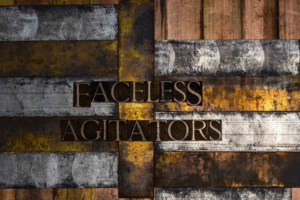 Photo of real authentic typeset letters forming Faceless Agitators text on vintage textured silver grunge copper and gold background - Photo, Image