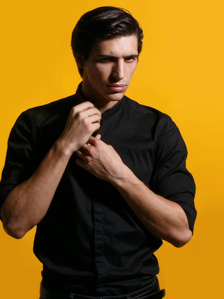 Portrait of a confident handsome young man in black clothing on yellow background. Vertical view. - Foto, afbeelding