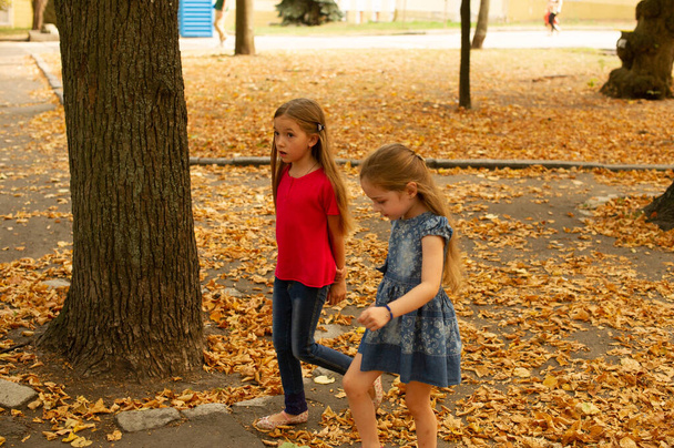 Schwestern, Outdoor Foto von zwei kleinen Mädchen. Zwei kleine Mädchen gehen an der Hand durch den Park. Schwestern für einen Spaziergang im Sommer oder Herbst auf der Straße. Freundinnen, Kinder, Natur. Familienkonzept. - Foto, Bild