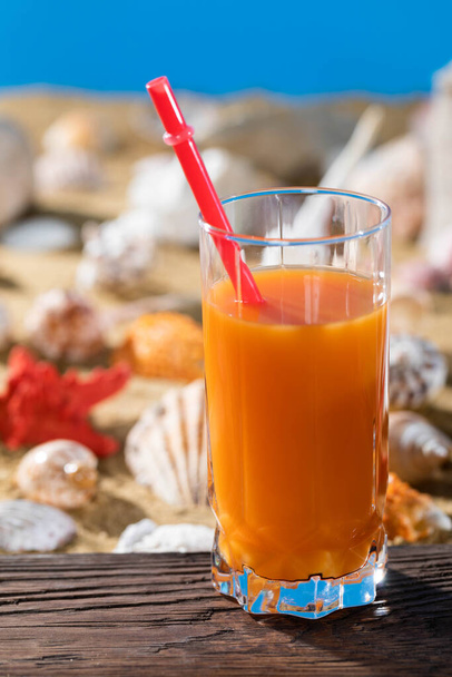 Fresh orange juice. A sandy beach on the shores of a cool sea. Brown platform board. - Foto, imagen