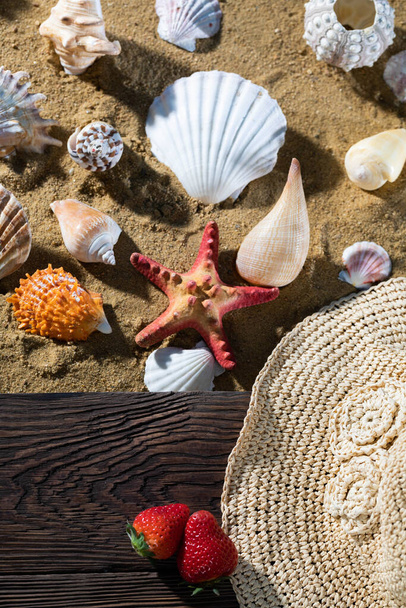 Sea beach full of various shells. Sandy beach. Two ripe strawberries. Summer hat. - Foto, immagini
