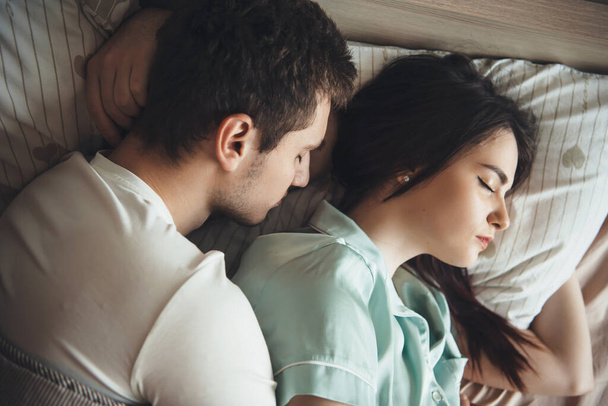 Krásný kavkazský pár spící spolu v posteli objímající a odpočívající - Fotografie, Obrázek
