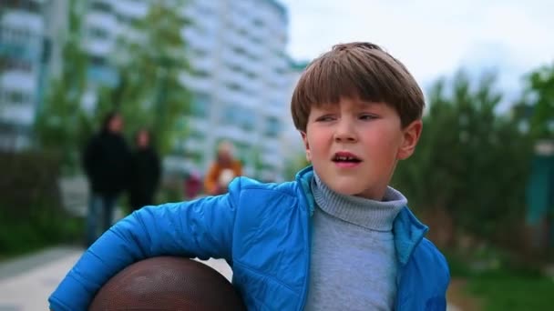 Een kleine jongen die op straat loopt en basketbal vasthoudt. - Video