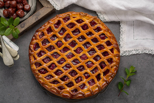 Домашній відкритий кислий вишневий пиріг, смачний солодкий десерт, поданий на сірому столі вид зверху
 - Фото, зображення
