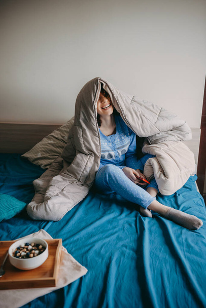 朝のベッドに座っている白人女性は、健康的なシリアルを食べるキルトで覆われています - 写真・画像