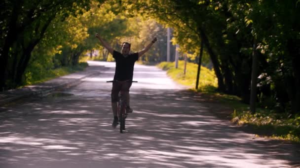 Young man riding a bike with his fist raised up - Materiał filmowy, wideo