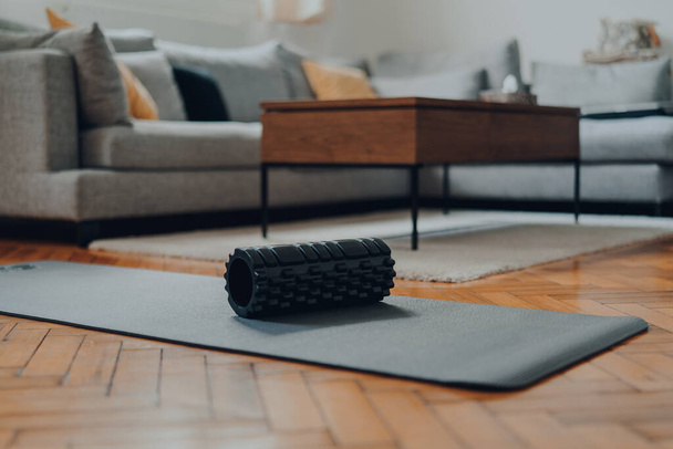 Rolo de espuma preta resistente em um tapete de fitness, interior de uma sala de estar moderna, foco superficial seletivo
. - Foto, Imagem