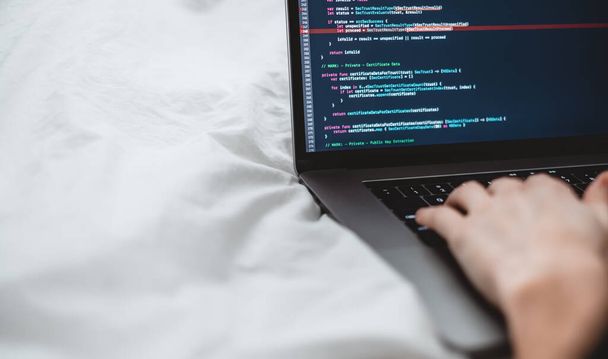 Female programmer writes program code on a computer laptop in the bed .  - Photo, image