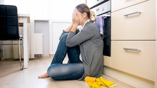 Mujer joven trastornada y estresada sentada en el suelo en la cocina y llorando
 - Foto, imagen
