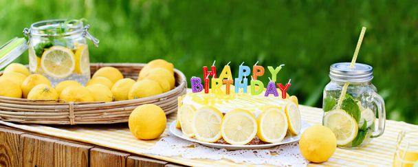 Birthday cake with happy birthday candles. Lemonade birthday party at summer park. food, celebration and festive concept. Mason jar glass of lemonade with lemons and straw. - Photo, Image