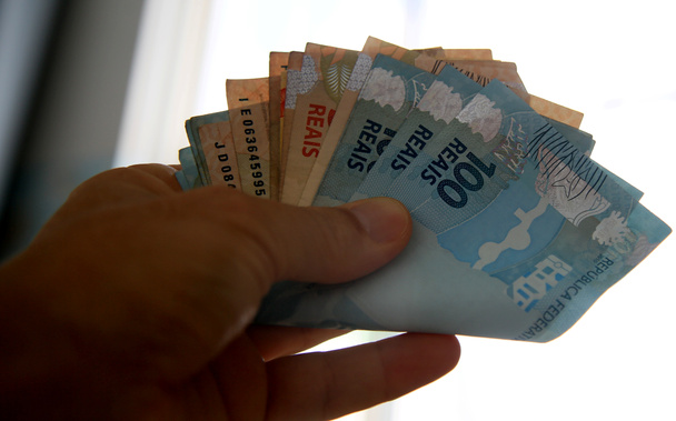 Сальвадор, Баия / Бразилия - 28 марта 2020 года: рука держит банкноты реальных банкнот, валюта используется в Бразилии
. - Фото, изображение