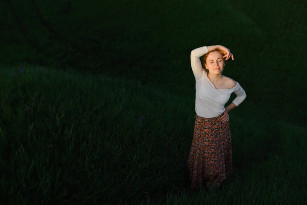 Retrato de una hermosa mujer con falda roja y blusa blanca. Posando en un campo al atardecer
. - Foto, Imagen