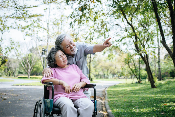 Idősebb férfi gondozza a fogyatékkal élő feleséget a tolószékében.. - Fotó, kép