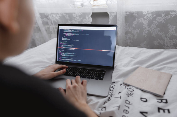 Young female programmer writes program code on a computer laptop in the bed .  - 写真・画像