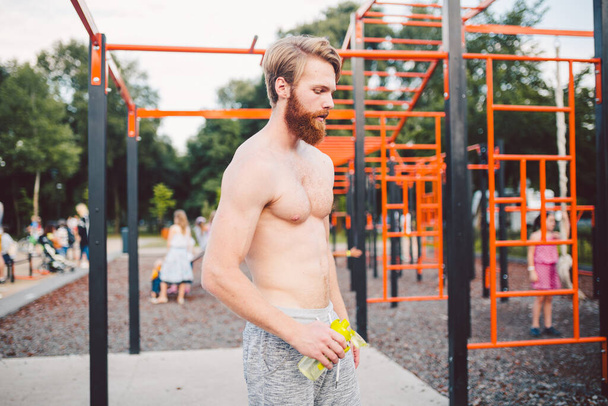 Sporty muscular man drinking water from sport bottle after workout at street gym. Thirsty man drinking water after training outdoor. Fitness, sport, lifestyle concept. Stay hydrated and healthy. - Photo, Image