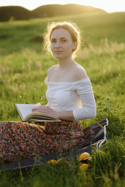 Молода дівчина читає книжку в траві під час заходу сонця. Літнє відчуття
 - Фото, зображення