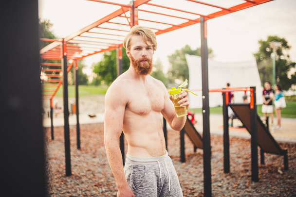 Athlete relaxing after intense workout, drinking water. Young strong sportsman male drinking water from bottle during outdoor fitness workout. care body hydration. sport and health. - Foto, imagen