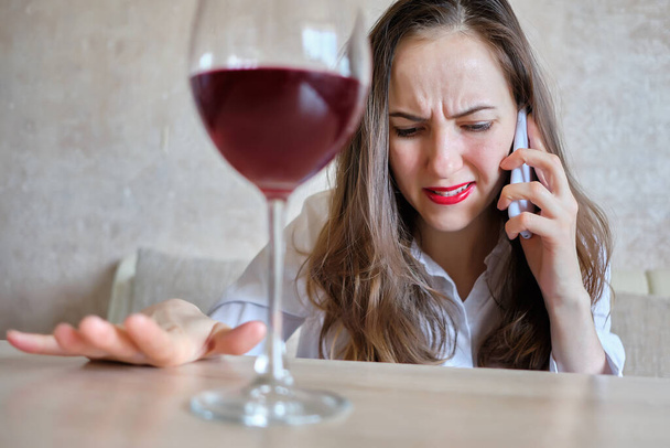 Wütendes Mädchen spricht auf einem Smartphone, während es Wein aus einem Glas trinkt - Foto, Bild