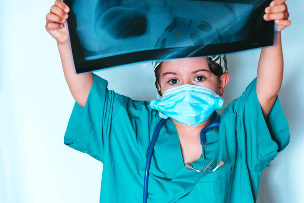 niedliches Kind spielt Arzt verkleidet als Chirurg bei der Untersuchung eines Röntgenbildes - Foto, Bild
