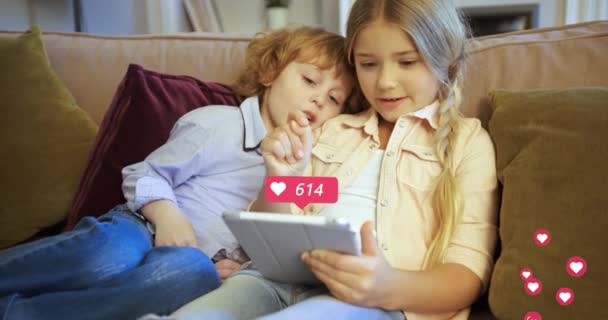 Caucasian kids, boy and girl sitting on sofa at home and using tablet device. Hearts counting in social media. Little children, sister and brother on couch playing on computer. Reactions in internet. - Filmagem, Vídeo
