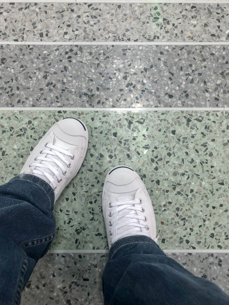 Zapatos blancos con jeans sentados en el parque.Pie y piernas vistas desde arriba.Selfie ideal para cualquier uso
. - Foto, imagen
