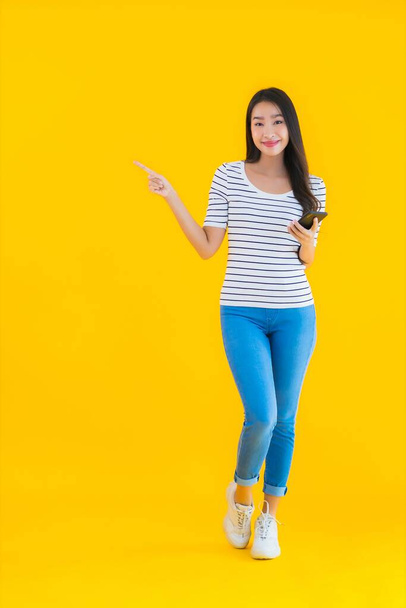 肖像画美しい若いアジアの女性の笑顔幸せな使用スマートフォン上の黄色隔離された背景 - 写真・画像
