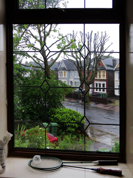 día lluvioso en una típica calle inglesa detrás de una ventana acristalada rizada y raquetas de bádminton se encuentran en el alféizar de la ventana. Foto de alta calidad
 - Foto, Imagen