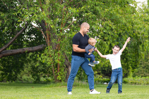 Батько грає з маленьким сином, обіймаючи дитину в парку в теплий літній день. Щаслива концепція дитинства. Щастя і гармонія сімейного життя. Відмінний сімейний відпочинок
.  - Фото, зображення