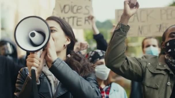 Ładna młoda, biała dziewczyna krzyczy w megafonie, stojąc wśród ludzi protestujących przeciwko rasizmowi i brutalności policji. Mieszane rasy męskie i żeńskie protestujące. - Materiał filmowy, wideo