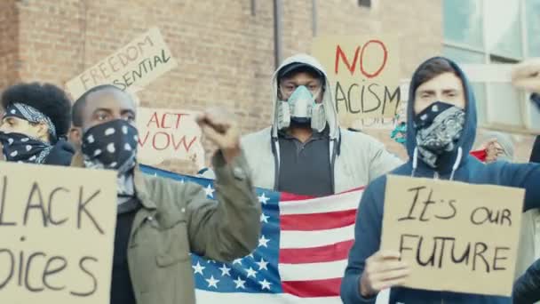 Afrikai-amerikai és kaukázusi férfiak lélegeztetőgépekben és maszkokban amerikai zászlókkal, akik jelszavakat kiabálnak, és részt vesznek a feketék emberi jogainak és egyenlőségének demonstrációjában. Megnyilvánulás az USA-ban. - Felvétel, videó