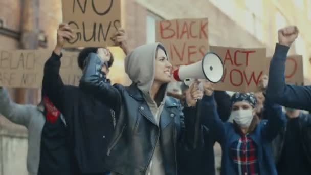 Giovane donna caucasica bella in cappuccio protestando in mezzo alla folla multietnica di manifestanti e urlando motti in megafono. Ragazza all'avanguardia nella manifestazione per i diritti umani
. - Filmati, video