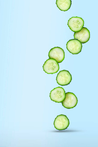 A lot of sliced fresh cucumber slices fall on a blue background. The concept of flying vegetables, food levitation. Vertical with copy space for text. - Foto, imagen