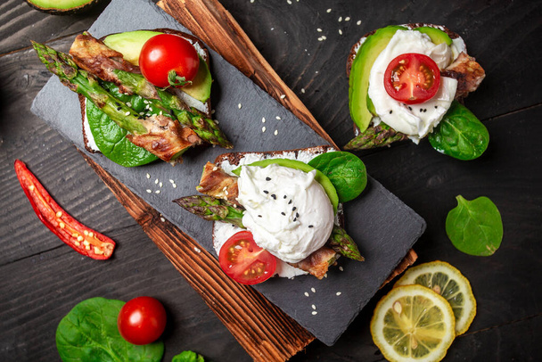 snack toasts with avocado, asparagus and fried egg. Food recipe background. Close up. - Photo, Image