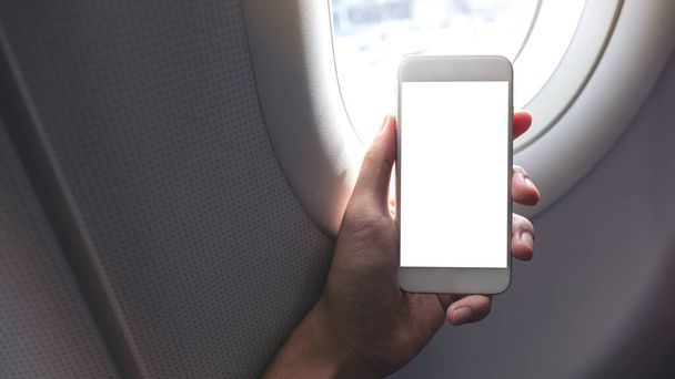 Boş masaüstü ekranı olan beyaz bir telefonu uçak penceresinin yanında tutan bir elin görüntüsü - Fotoğraf, Görsel