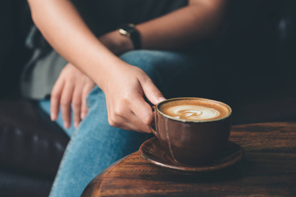 Zbliżenie obraz kobiety trzymającej filiżankę kawy na zabytkowym drewnianym stole w kawiarni - Zdjęcie, obraz
