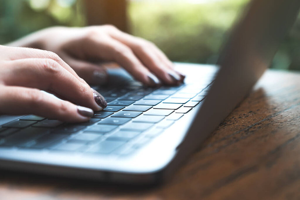 Imagen de cerca de las manos de la mujer trabajando y escribiendo en el teclado del ordenador portátil en la mesa de madera con fondo verde de la naturaleza
 - Foto, Imagen