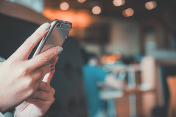 Imagen de cerca de las manos de una mujer sosteniendo, usando y mirando el teléfono inteligente en la cafetería con fondo borroso
 - Foto, imagen