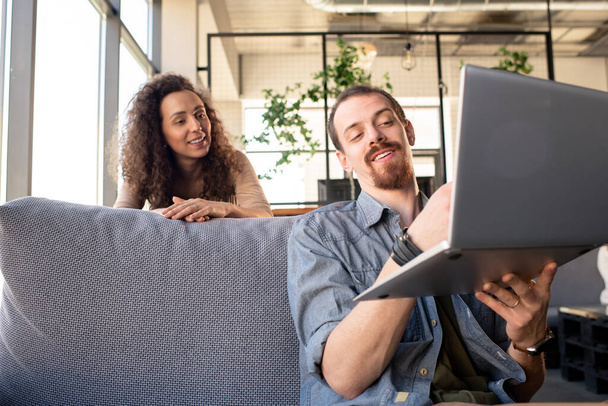 Genç, gülümseyen sakallı adam iş sırasında laptopuna işaret ederken karısına restoranları için yeni ekipmanlar gösteriyor. - Fotoğraf, Görsel