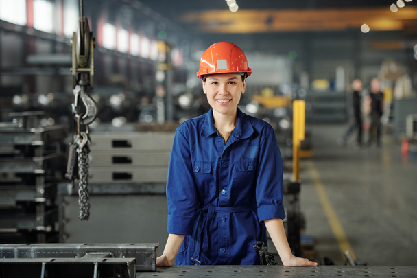 Портрет усміхненого молодого азійського фахівця з металургії в синіх накладках, що стоїть за столом у промисловому цеху. - Фото, зображення