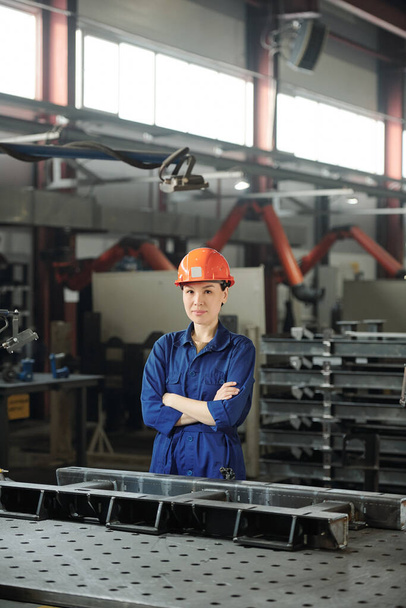 Портрет привлекательного азиатского специалиста по металлообработке в каскаде, стоящего за столом с металлическими деталями в мастерской
 - Фото, изображение