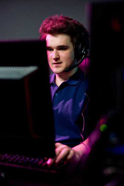 Mladý muž video hráč s headset držet ruku na klávesnici při pohledu na obrazovce počítače během hry v tmavé místnosti - Fotografie, Obrázek