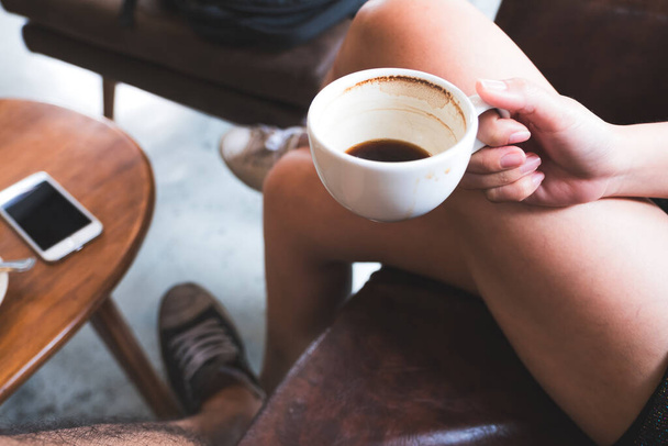 Closeup image of a woman holding black coffee cup while sitting on sofa with friend in cafe - Foto, afbeelding