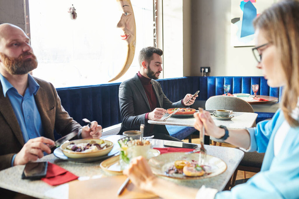 Knappe jonge zakenman die salade eet en telefoon checkt in een modern café - Foto, afbeelding