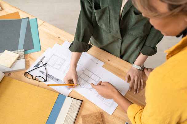 Dwie kreatywne projektantki pochylające się nad stołem podczas dyskusji nad papierami ze szkicami nowego domu lub mieszkania na spotkaniu roboczym - Zdjęcie, obraz